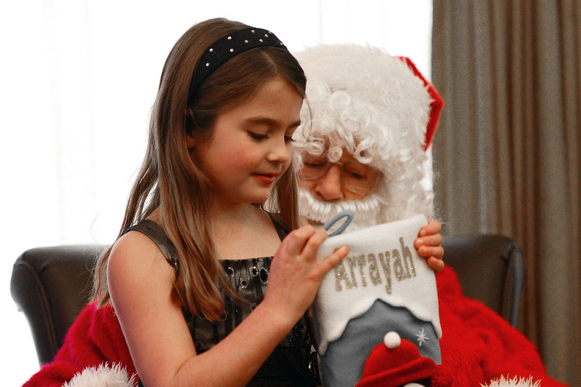 Arrayah Jaeger, 8, opens gifts purchased by the residents of Prestige Assisted Living on Santa&#146;s lap, portrayed by Prestige resident RJ Kraft in Kalispell on Wednesday, Dec. 13. (Casey Kreider/Daily Inter Lake)