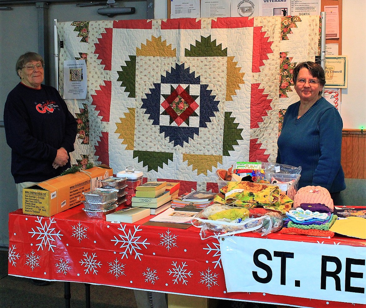 Mary Eldridge (left) made and donated a quilt to be raffled off with funds raised for the St. Regis Senior Center. Mary Burrows, far right, helped to sell tickets at the holiday bazaar. (Kathleen Woodford/Mineral Independent).