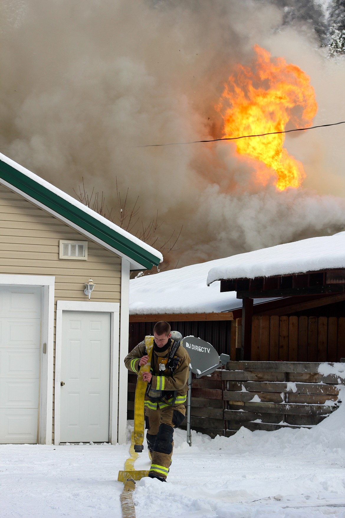 A firefighter carries a hose line away from the home as crews establish a second front at the rear of the house.