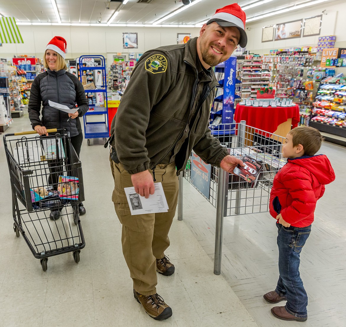 Lincoln County Sheriff&#146;s Deputy Brad Dodson helps Bentley Seefeldt shop for Christmas gifts at Shopko in Libby during Shop With a Cop Tuesday, Dec. 19, 2017. Dodson&#146;s wife Kaide Dodson, left, assistant principal at Libby Middle/High School, helped shop. (John Blodgett/The Western News)