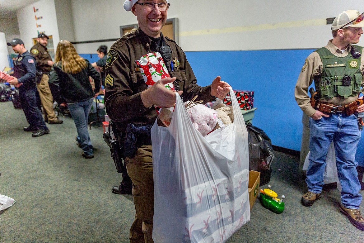 Lincoln County Sheriff&#146;s Deputy Boyd White carries a bag full of Christmas gifts at Asa Wood School in Libby during Shop With a Cop Tuesday, Dec. 19, 2017. (John Blodgett/The Western News)