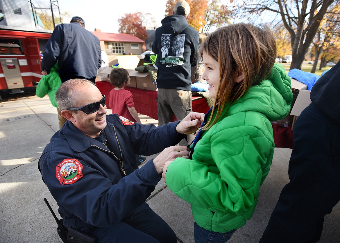 Captain Kirk Pederson helps Izzabela Lamantia, a first grader at Russell Elementary, into a new coat on Tuesday, October 24, in Kalispell. Members of the Kalispell Fire department were at the school participating in Operation Warm for the fourth year. They will also be giving out coats at Elrod and Hedges on Friday.(Brenda Ahearn/Daily Inter Lake)