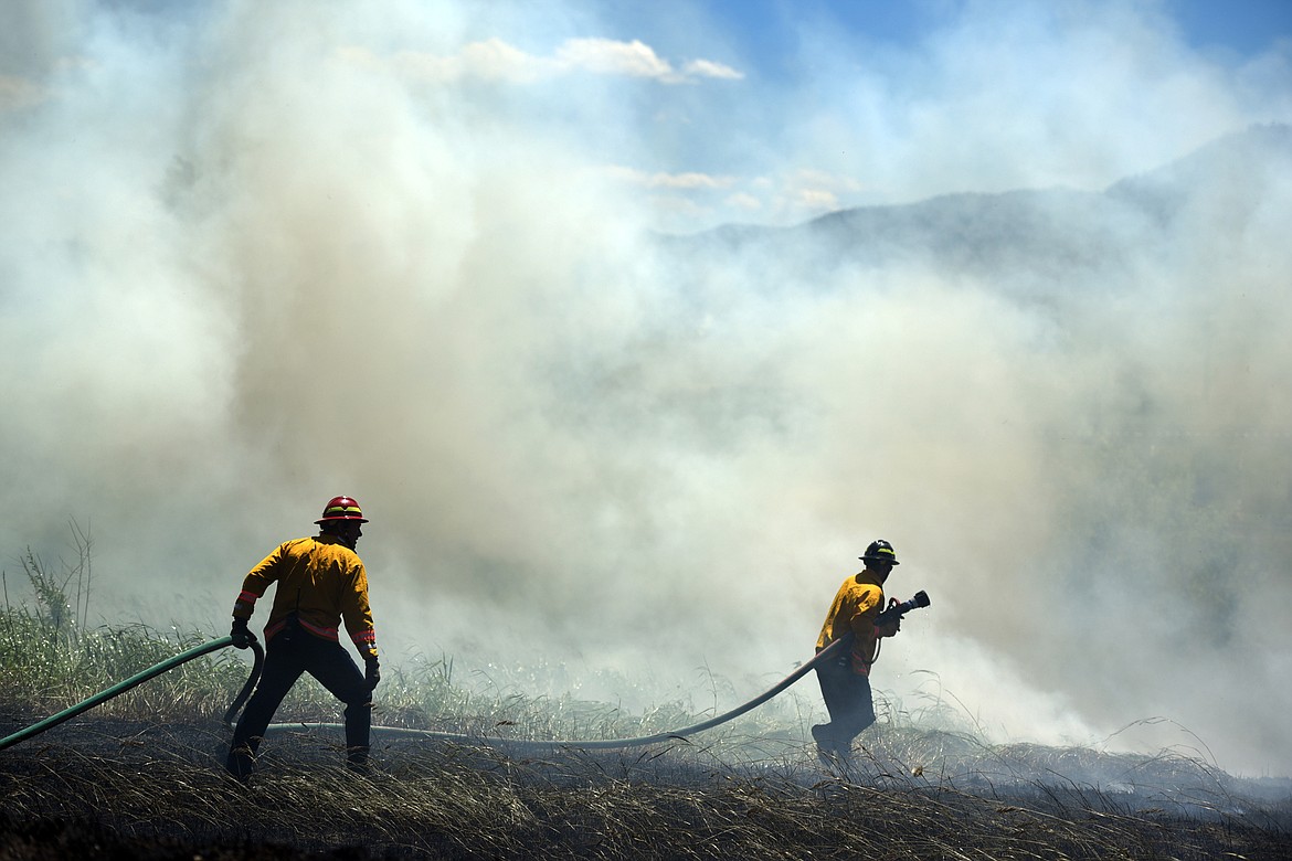 Kalispell Fire fighters Adam Smart, left and Jake Hall right, make their way further into the scene of a grassfire near Apple Way on Wednesday afternoon, June 21, in Kalispell.(Brenda Ahearn/Daily Inter Lake)