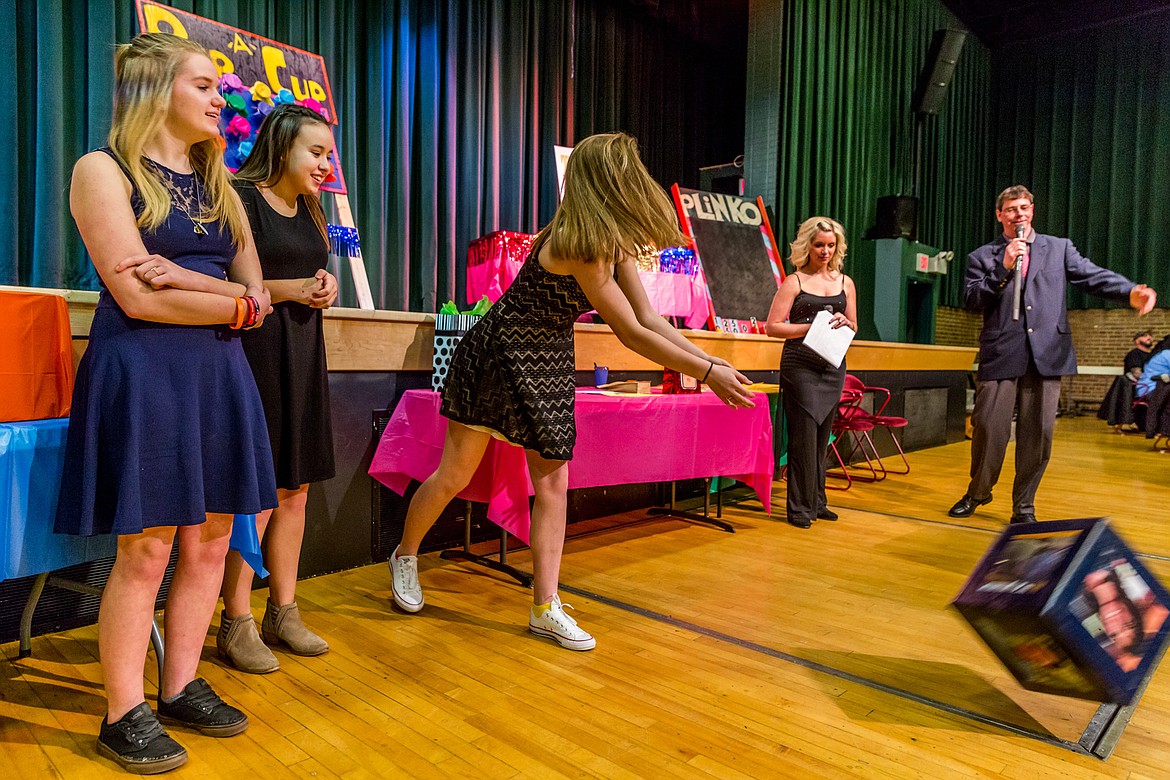 Jessika Jones, center, rolls a &#147;die&#148; during the &#147;Heads and Tails&#148; game at the Libby Chamber of Commerce Banquet Saturday night at the Libby Memorial Events Center Saturday. Assisting her are Paige Chapel, left, and Marissa Wood. Patricia Morford and Brent Orr, background, play the roles of Vanna White and Bob Barker, respectively. (John Blodgett/The Western News)