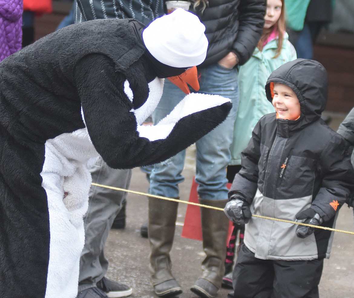 A Penguin offers Johnny Stebbins a high-five before the start of the Whitefish Winter Carnival Grand Parade. (Heidi Desch/Whitefish Pilot)