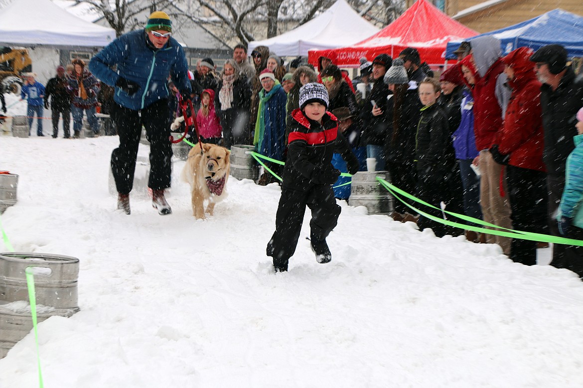 (Photo by CAROLINE LOBSINGER)A youngster leads the way to encourage this less-than-enthused competitor to race down one of two K9 Keg Pull tracks at Sunday's Winter Carnival event.