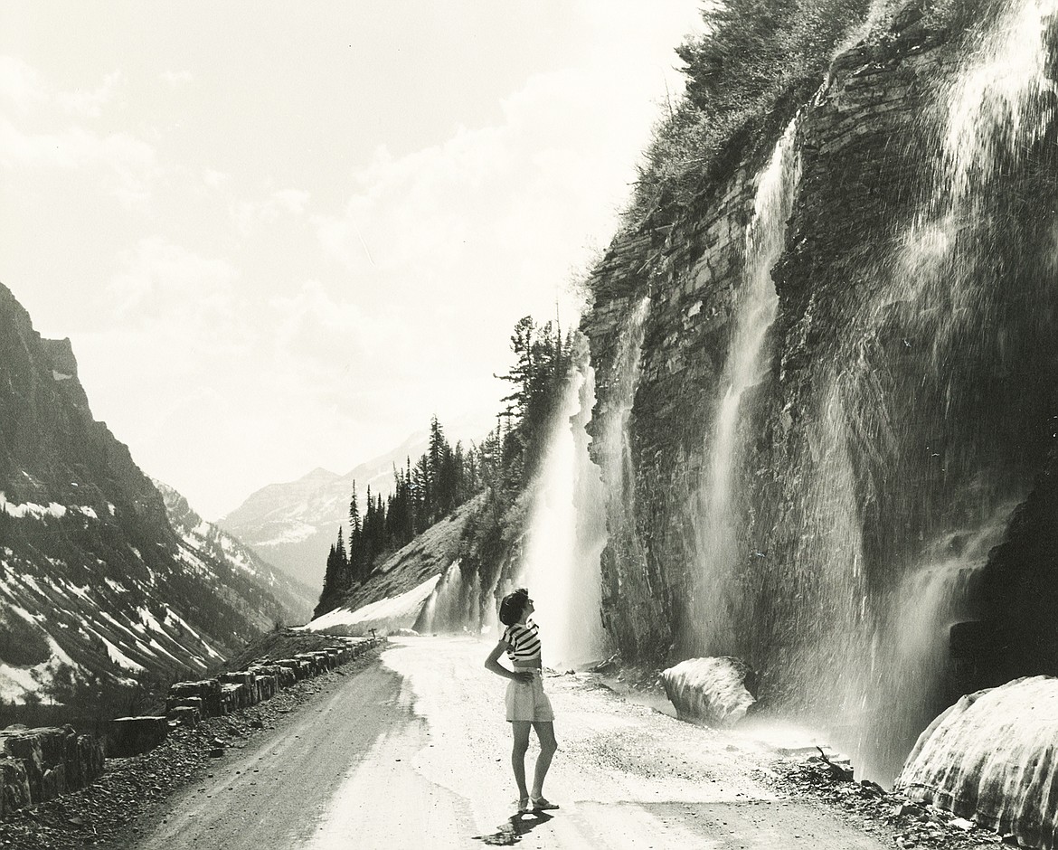 Sheila Lacy (Morrison) stands under the Weeping Wall on Going-to-the-Sun Road in Glacier National Park in the 1950s.