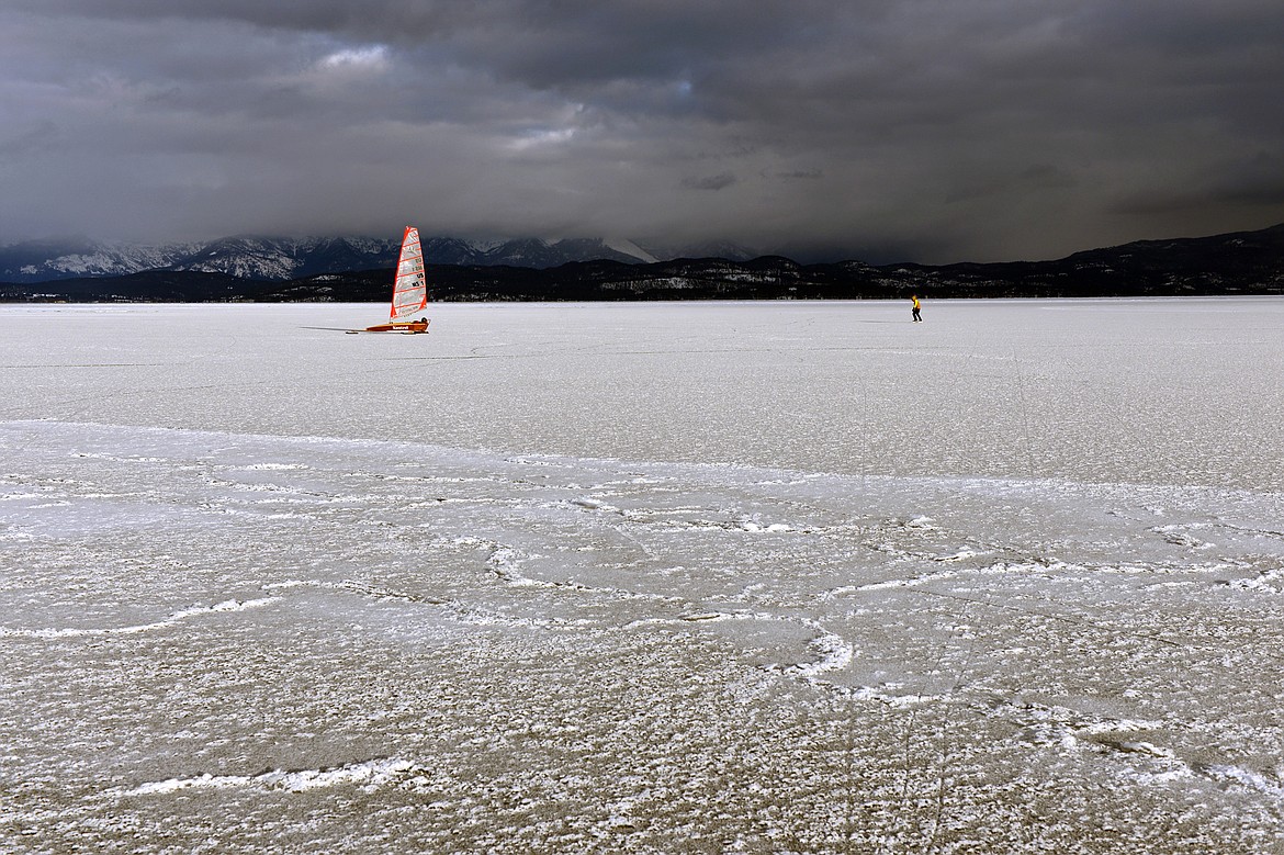 John Eisenlohr, left, of Lakeside sails his ice boat while Greg Fortin of Columbia Falls ice skates across the frozen surface of Flathead Lake in Lakeside on Feb. 23. (Casey Kreider/Daily Inter Lake)