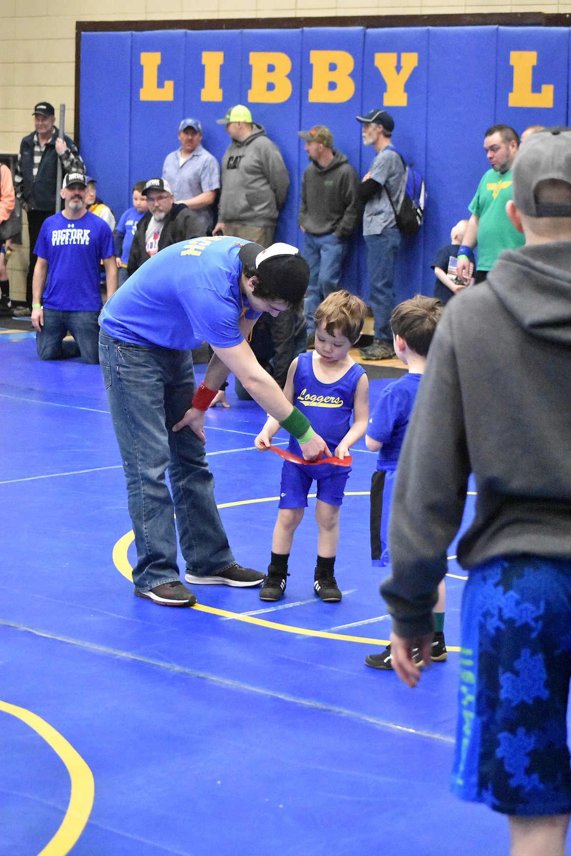 Referee Tim Carvey shows helps Waylon Edwards with the ankle band that indicates a wrestler&#146;s color during the Kootenai Klassic, March 3.