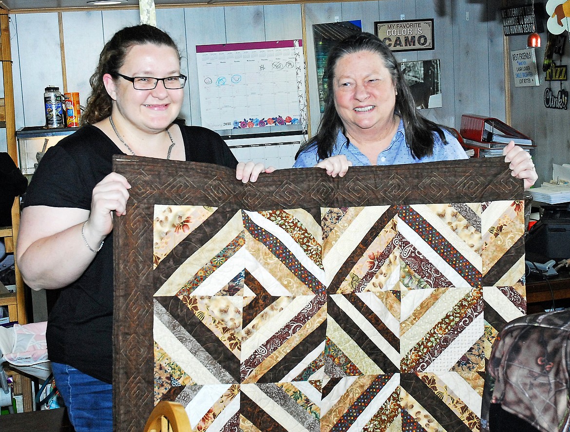Presenting the quilt to Amy Cielke (left) is Cabin Fever Quilters Guild President Karlene Zunino (right). The Guild provides quilts to families in need and the Cielke family recently lost their home to a house fire near Haugan. (Photo courtesy Cabin Fever Quilters Guild)