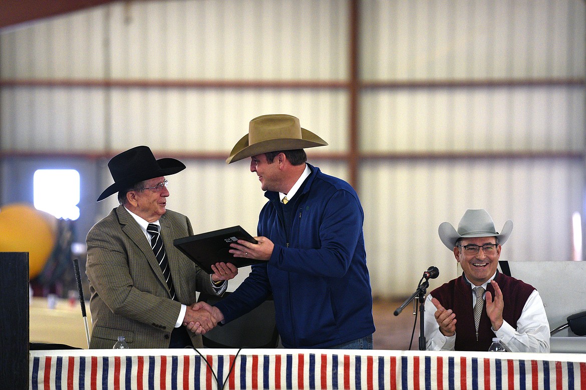 Brett Spader, center, with the American International Charolais Association, gives Buddy Westphal, left, an award commemorating 55 years in the Charolais cattle business prior to the 50th annual Bull Sale at Valley View Charolais Ranch in Polson on Saturday, March 24. At right is auctioneer Rick Machado. (Casey Kreider/Daily Inter Lake)