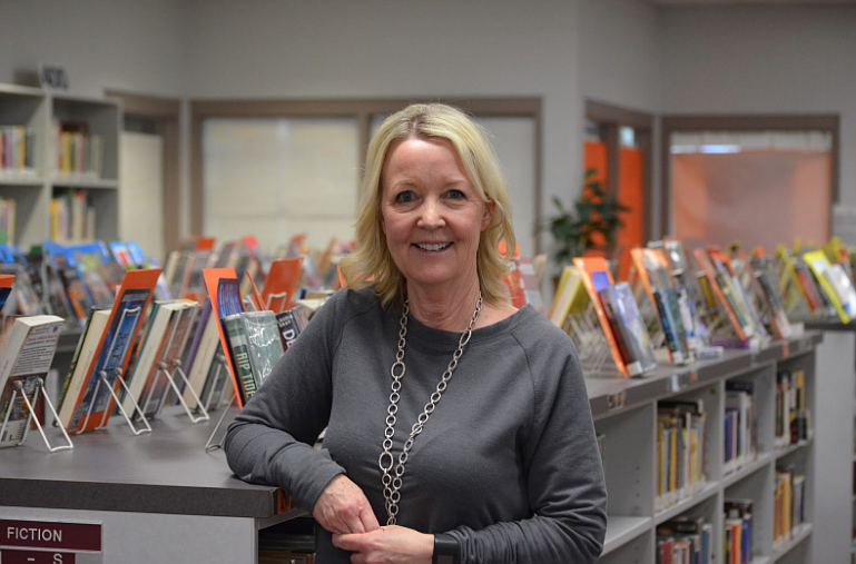 Sue McLauchlin, the librarian at Post Falls High School, stands in front of her organized fictional reading section.