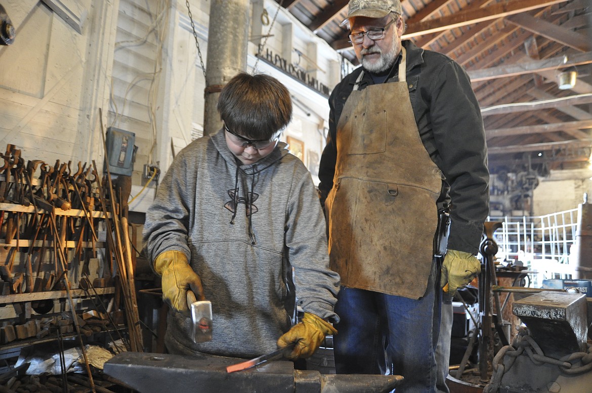 AS JACKSON Sorrell, 9, pounds his metal masterpiece into shape, Chuck Thuemler watches. Sorrell attended a free blacksmithing workshop offered by the Miracle of America Museum in Polson on Saturday, April 7. (Ashley Fox/Lake County Leader)