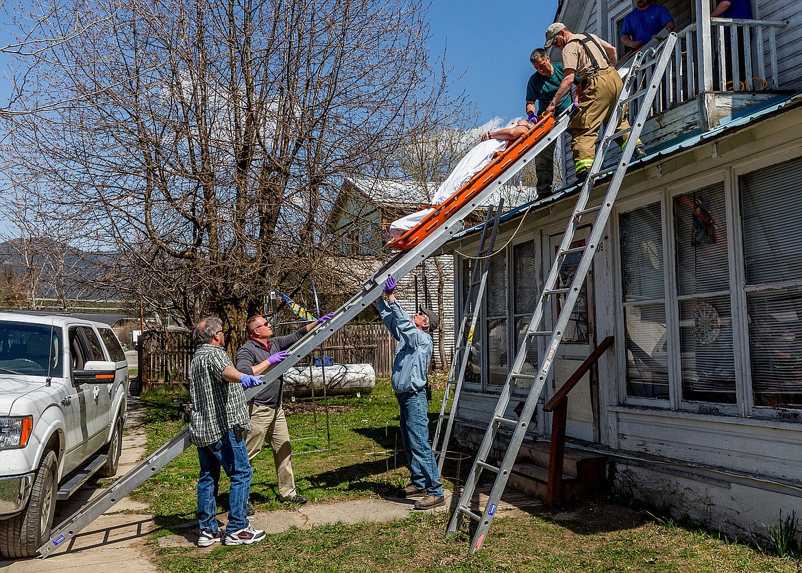 Libby volunteer firefighters help volunteer ambulance personnel retrieve a man who was reported to have fallen inside a residence in the 400 block of Montana Avenue Wednesday afternoon. According to Fire Chief Tom Wood, the fire department was dispatched to assist with ladders and a basket stretcher because “a very narrow and steep stairway” inside the home prevented ambulance members from taking him out that way. “The patient needed to be laying flat, so they couldn’t bring him down on the stretcher in the extended manner,” Wood said Thursday via email. “Normally they can sit a person up and bring them down tight stairs like those.” (John Blodgett/The Western News)