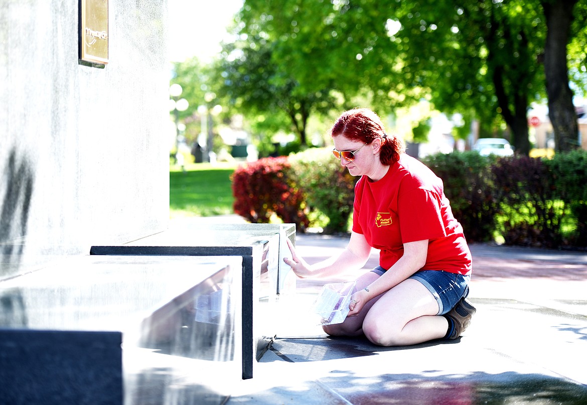 Cristina Woolley kneels to polish the base of the Veterans Memorial.