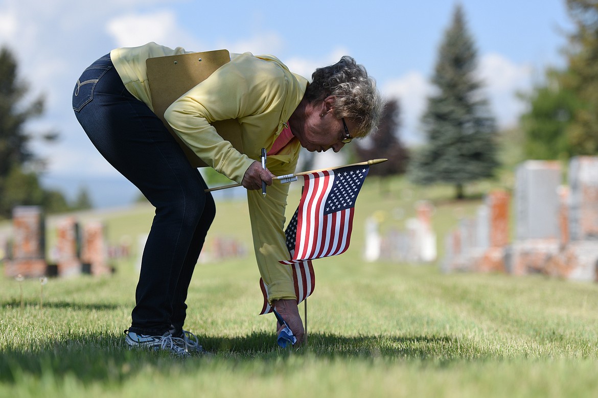 Jan Olson, secretary with the Chief Ignace Chapter of the National Society Daughters of the American Revolution, places an American flag and a smaller blue and white flag for past officers at the gravestone of Blanche A. Switzer in Conrad Memorial Cemetery in Kalispell on Friday morning. (Casey Kreider/Daily Inter Lake)