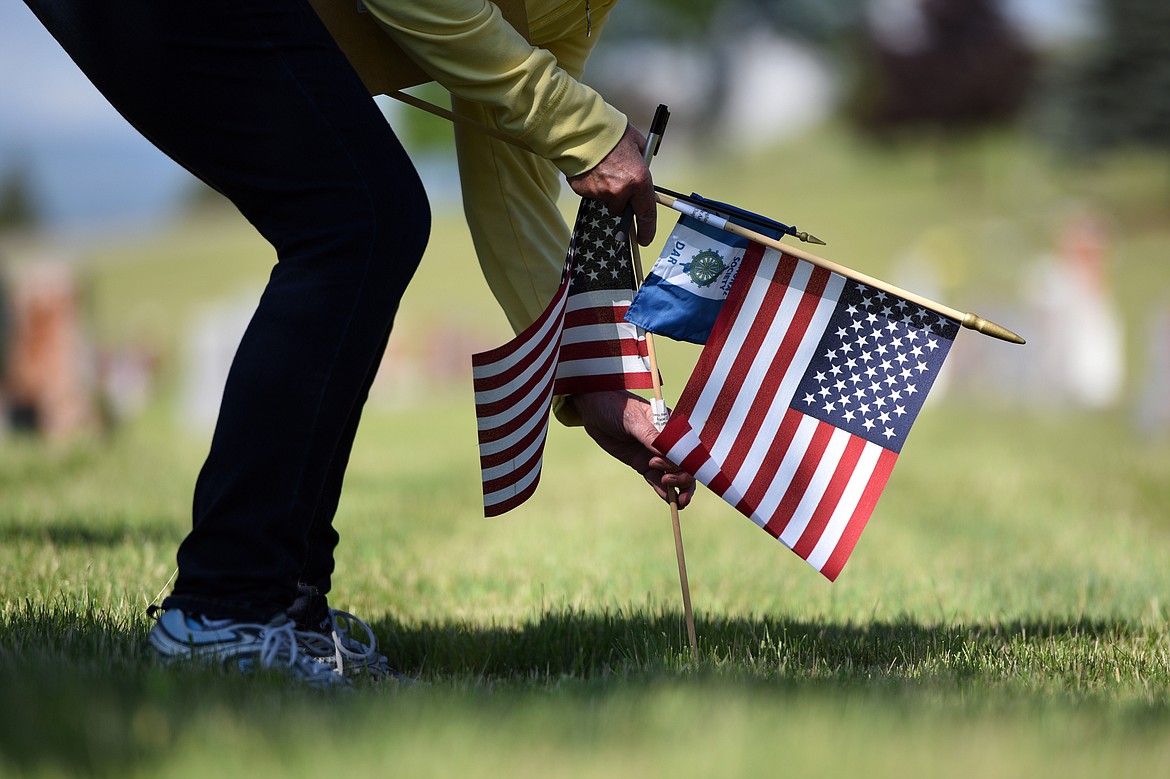 Jan Olson, secretary with the Chief Ignace Chapter of the National Society Daughters of the American Revolution, places an American flag and a smaller blue and white flag for past officers at the gravestone of Blanche A. Switzer.