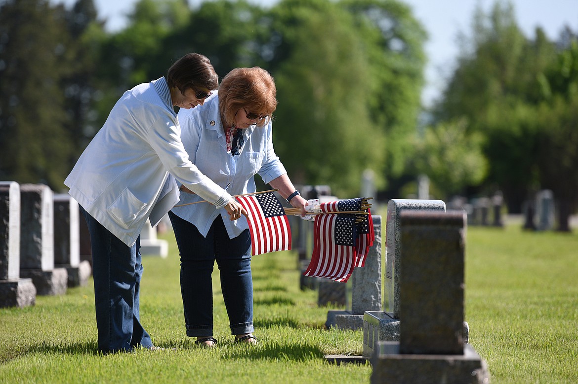 Pat Gillies, left, and Cate Webber, officers with the Chief Ignace Chapter of the National Society Daughters of the American Revolution, place an American flag at the gravestone of past member Laura Elsass in Conrad Memorial Cemetery in Kalispell on Friday morning. (Casey Kreider/Daily Inter Lake)