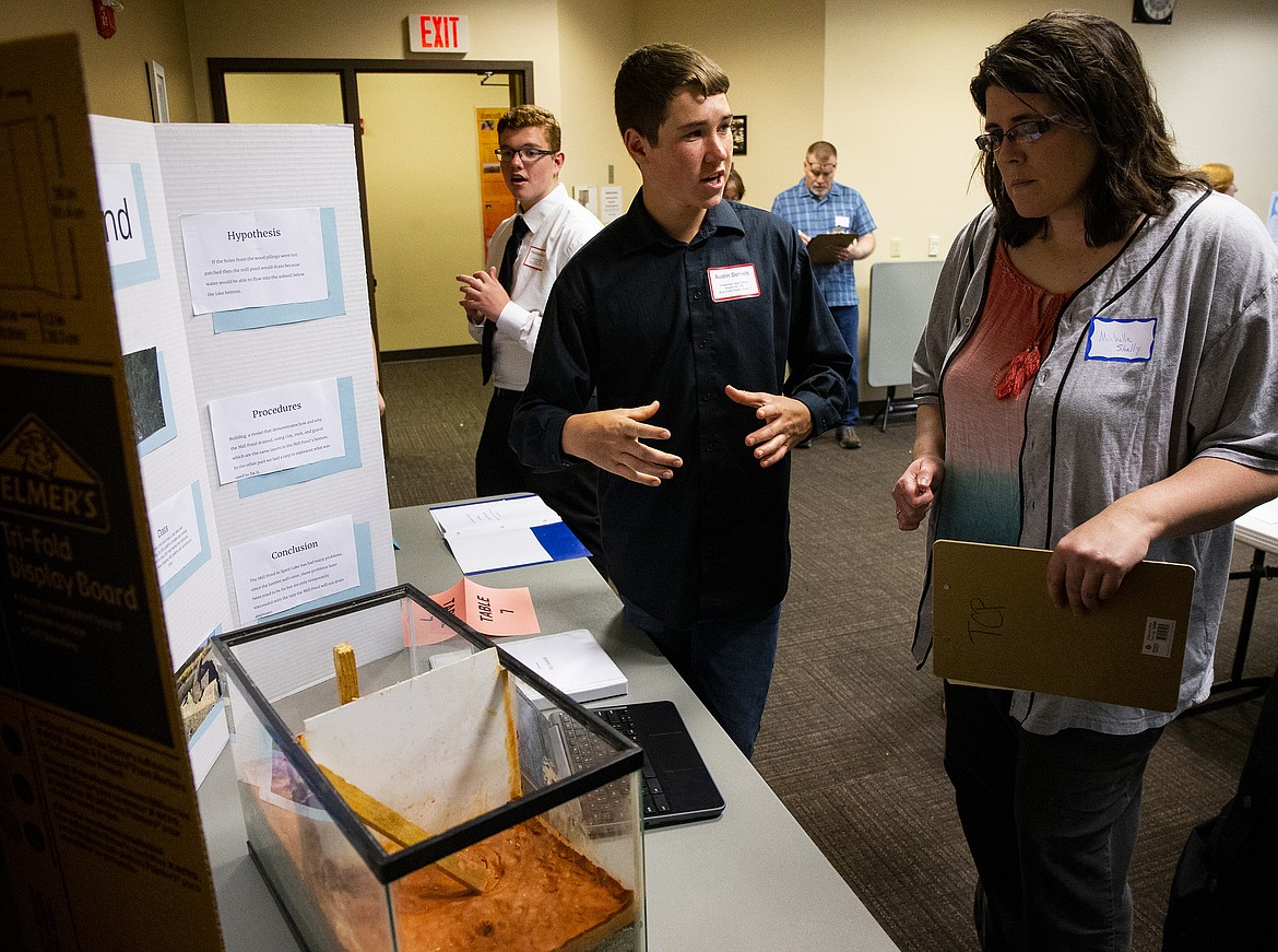 Timberlake High School student Austin Daniels describes the history of the Spirit Lake Mill Pond to Michelle Shelly. The fishtank display helps to show how wood pilings from the former Mill had been driven through the clay bottom and began to rot. (LOREN BENOIT/Press)