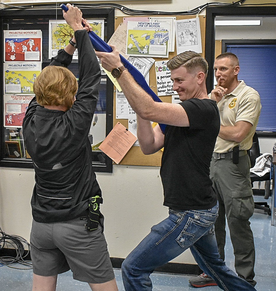 Libby School teacher Cindy Ostrem-Johnston, left, learns how to render a shooter incapable of inflicting injury with the help of Kalispell Police Officer Justin Turner, as U.S. Forest Service officer Jack Dittmann observes, Friday at Libby High School. Both officers are instructors with the Northwest Run, Lock, Fight Group. (Benjamin Kibbey/The Western News)