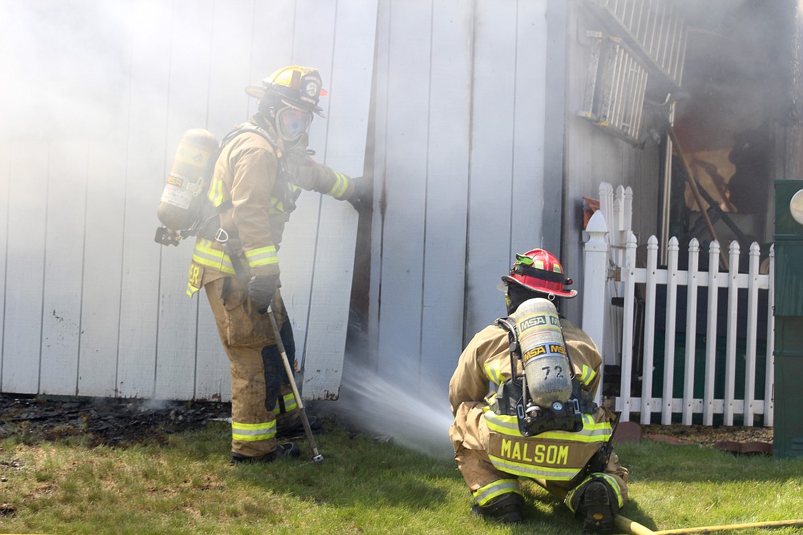 Firefighters Walcker and Malsom work to cool the glowing metal on the ground in the rear of the garage.