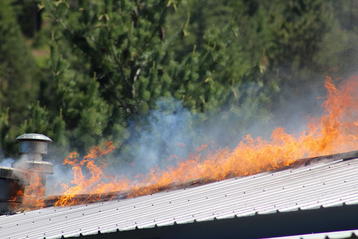 Fire creeps across the top of the home while being fanned/kept in check by the wind.