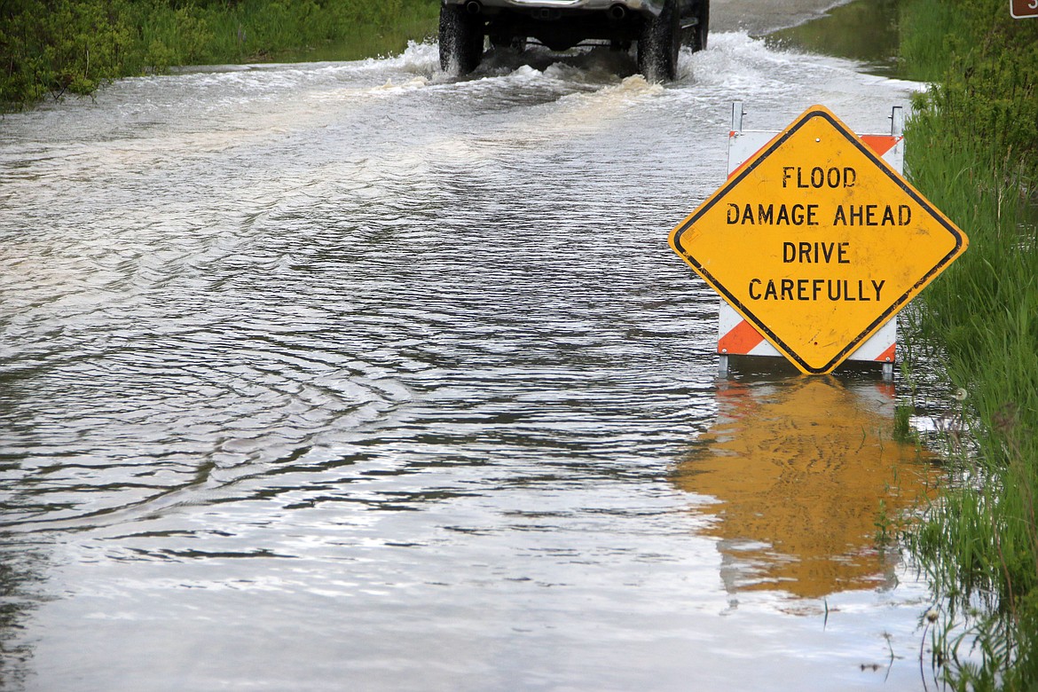 (Photo by MARY MALONE)
A car carefully makes its way through the water after the Priest River rose up across a private property and flooded across Lower Quartz Creek Road and into Peninsula Road, next to the Green Owl Tavern.