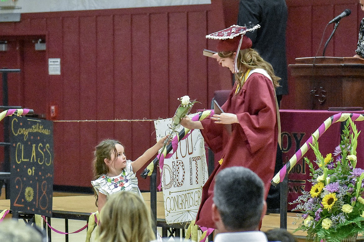Flower girl Embry Cairns hands a white rose to Troy High School graduate Kaylee Kidwell as she leaves the stage after receiving his diploma during graduation ceremonies on Saturday, June 2, 2018. (Ben Kibbey/The Western News)