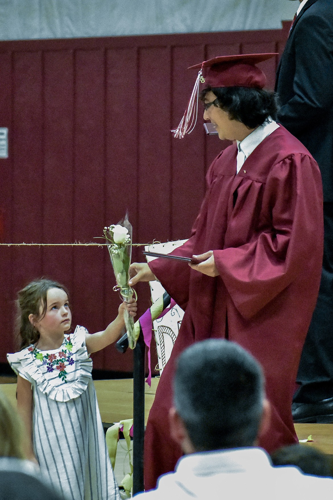 Flower girl Embry Cairns hands a white rose to Troy High School graduate Liam Hennsley as he leaves the stage after receiving his diploma during graduation ceremonies Saturday. (Ben Kibbey/The Western News)