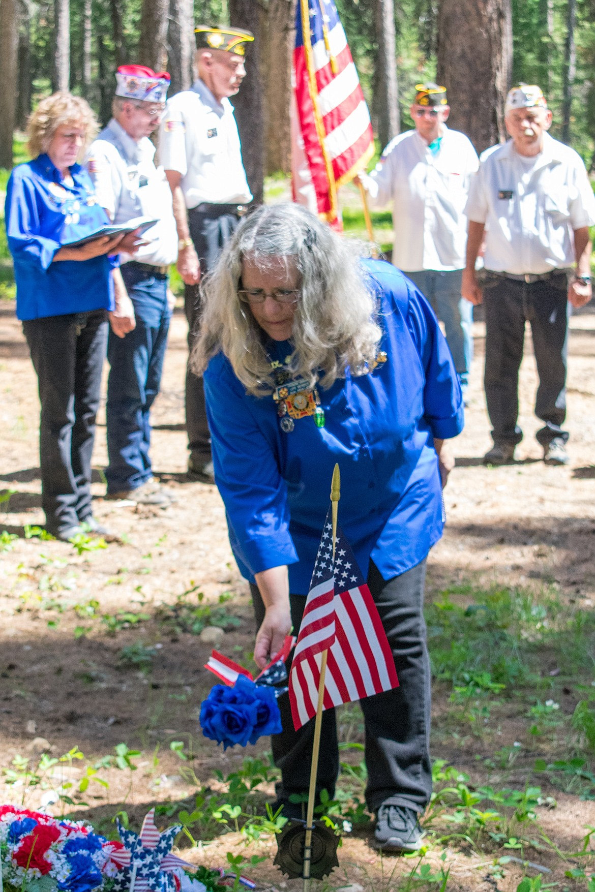 VFW John E. Freeman Post 5514 Auxiliary President Francine Ninneman places blue flowers symbolizing eternity and the immortalization of the deeds of deceased service members during the Memorial Day Service Monday at Boyd Cemetery in the Yaak. (Ben Kibbey/The Western News)