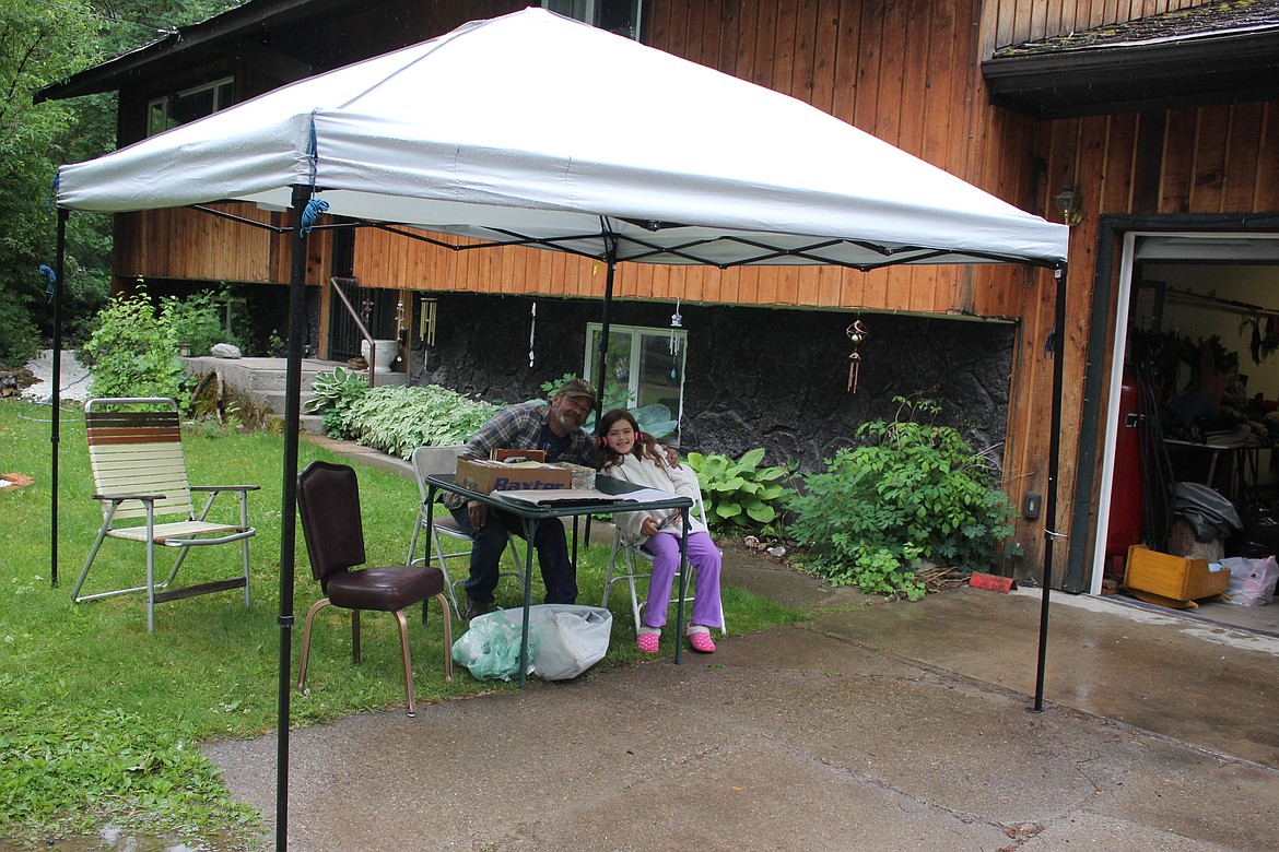 St. Regis resident Vince Triplett and granddaughter Marlee stay dry under a canopy on a rainy Saturday town-wide yard sale. (Kathleen Woodford/Mineral Independent)