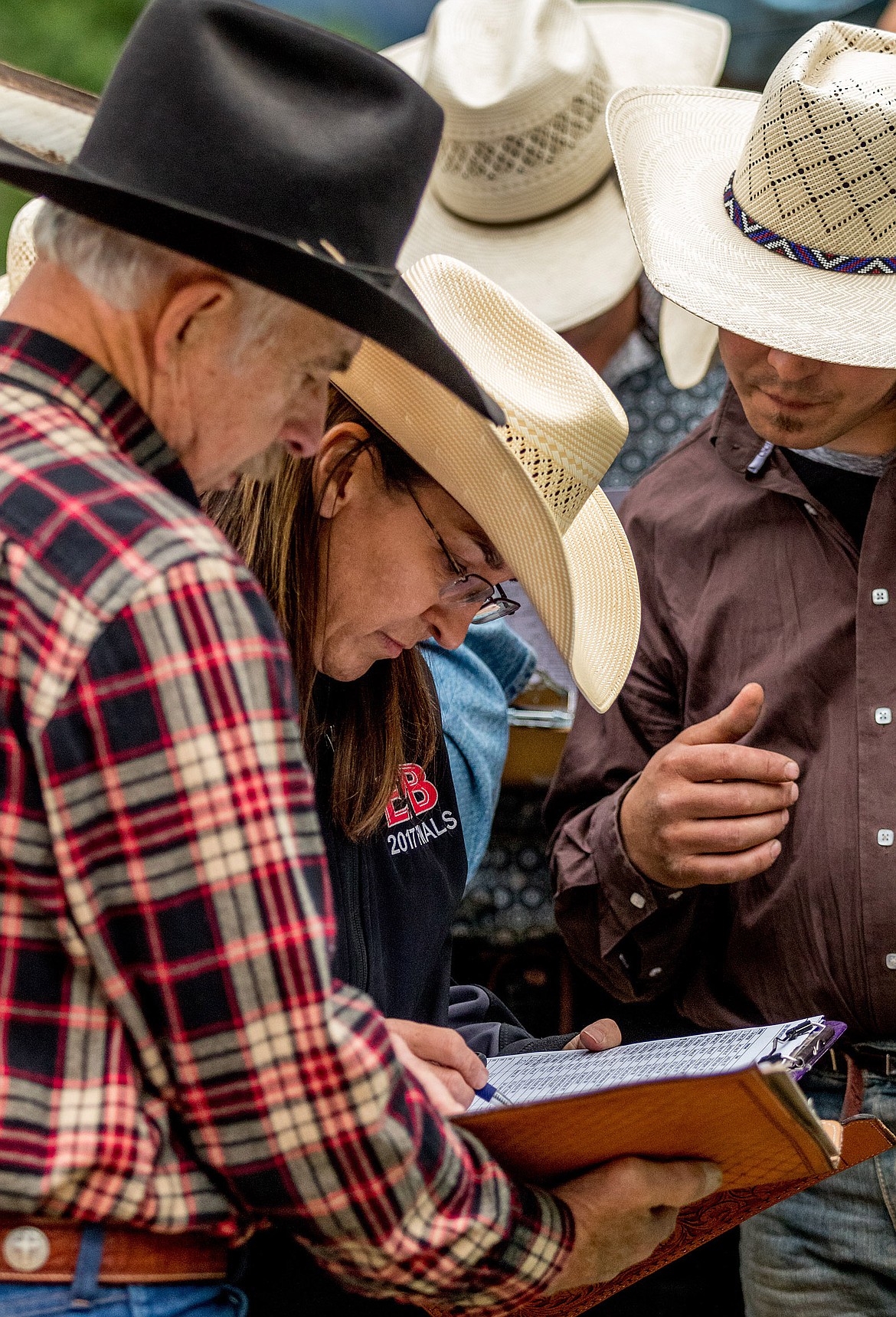 Sandy Mac, center, and Incredi-Bull committee chairman Brett Bronson, left, determine which riders had qualified to compete in the short round at Saturday night's event at J. Neils Park in Libby. (John Blodgett/The Western News)