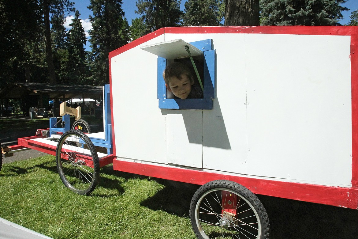 Sam Monter, 8, of Hayden, peeks out the little window on the mini travel trailer his big bro Alex, 14, built to drive in the Gizmotion parade Saturday in Coeur d'Alene City Park. Alex spent between 40 and 50 hours working on the wooden human-powered vehicle, which he painted red, white and blue for the Fourth of July. (DEVIN WEEKS/Press)