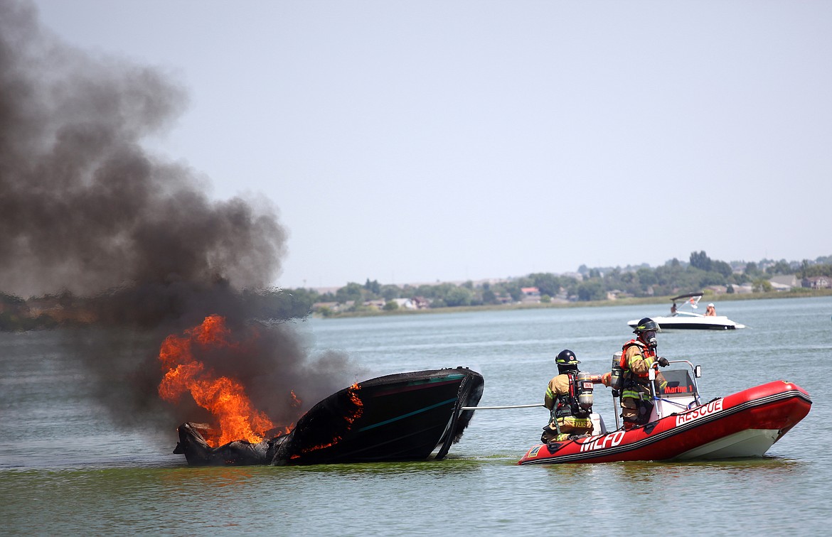 Rodney Harwood/Columbia Basin Herald
Moses Lake fire fighters tow a recreational boat that caught fire shortly after noon on Thursday near the dock at Blue Heron Park. The fire department brought the boat closer to the shore after letting it burn down in the middle of the lake to extinguish it with ground support. There were no injuries.