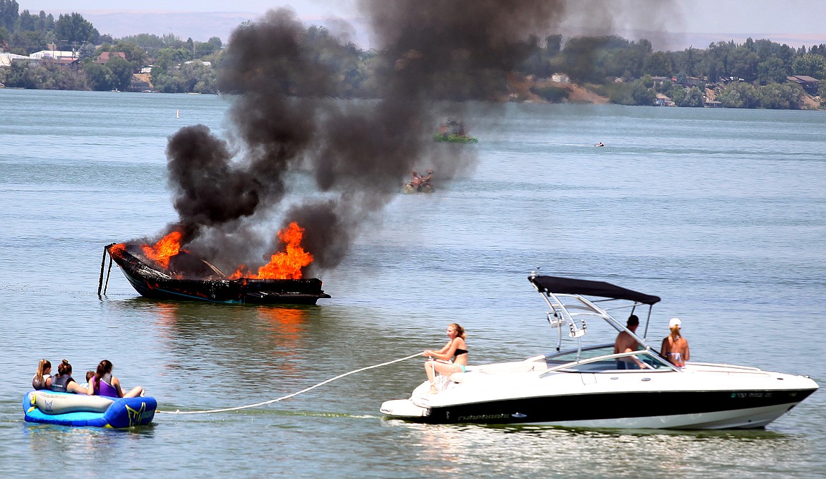 Rodney Harwood/Columbia Basin Herald
Boaters in the vicinity look on at a recreational boat that caught fire shortly after noon on Thursday near the dock at Blue Heron Park. Occupants were rescued and there were no injuries. Cause has yet to be determined.