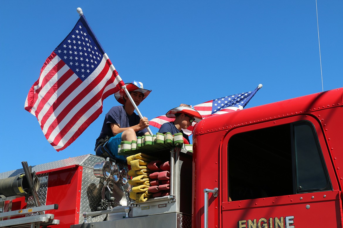 (Photo by CAROLINE LOBSINGER)A pair of parade participants ride atop a fire engine during the Sandpoint Lions' Grand Parade on the Fourth of July on Wednesday.