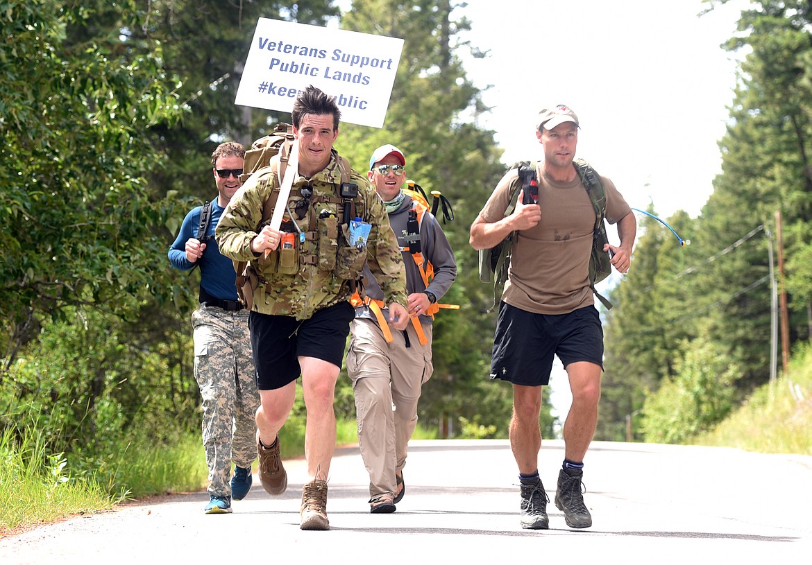 Anton Nygard, 29, of Missoula carries a sign that reads &#147;Veterans Support Public Lands&#148; as he and Andrew Person, 38, also from Missoula, and Charlie Cromwell, 37, from Bozeman, in blue and Mike Talia, 37, from Helena in gray, trek from Polebridge to Les Mason State Park along Whitefish Lake on July 2. The four completed the 60 kilometer walk, one kilometer for each national park.&#160;(Brenda Ahearn/Daily Inter Lake)