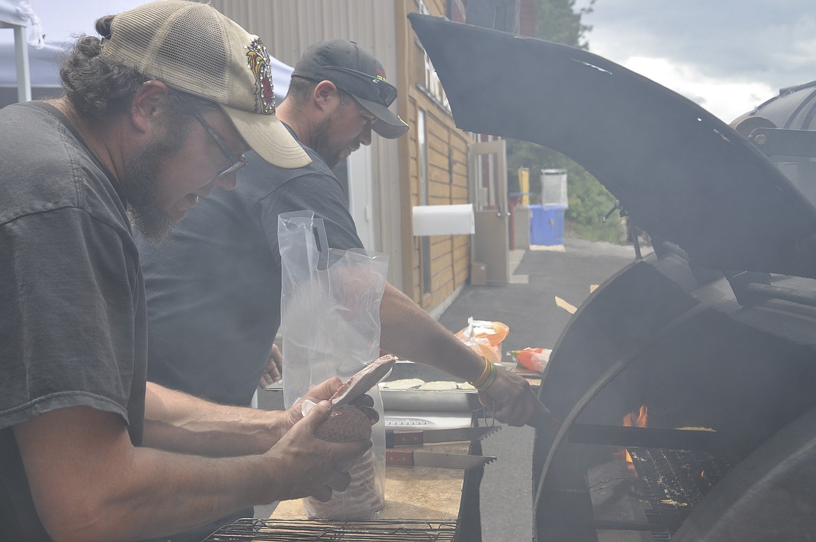 COOKING FOR THE Finley Point/Yellow Bay Fire Department barbecue are Teague Wilson, left, and Richard Peterson, right. Both men are volunteer firefighters with the department. (Ashley Fox/Lake County Leader)