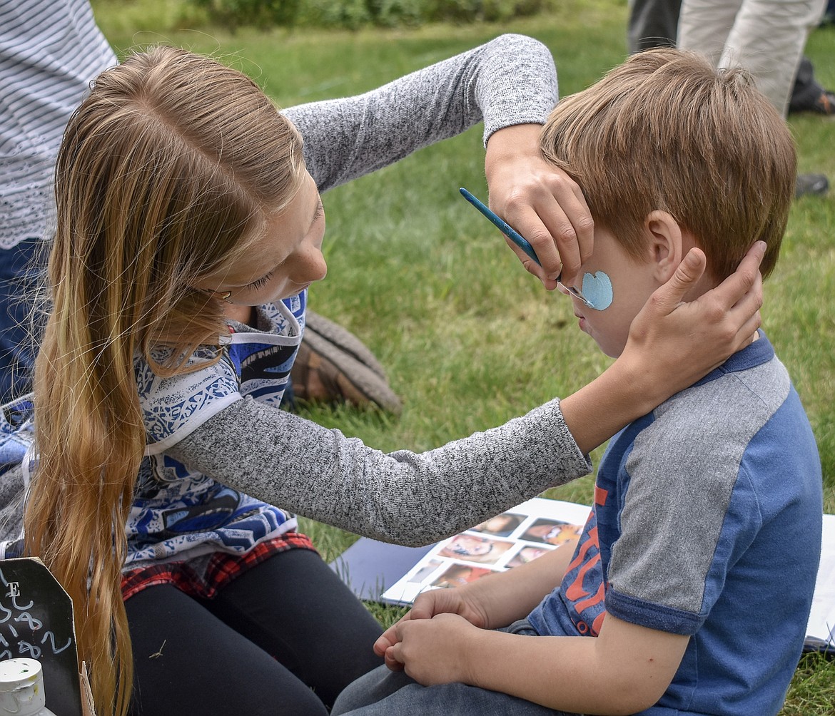 Ani Vick, who just finished fourth grade at the Yaak School, paints the face of Cliven Tucker, who was visiting the Yaak from Chicago with his family, during the sixth annual Yaak School Arts and Crafts Fair Saturday, June 30. 
(Ben Kibbey/The Western News)