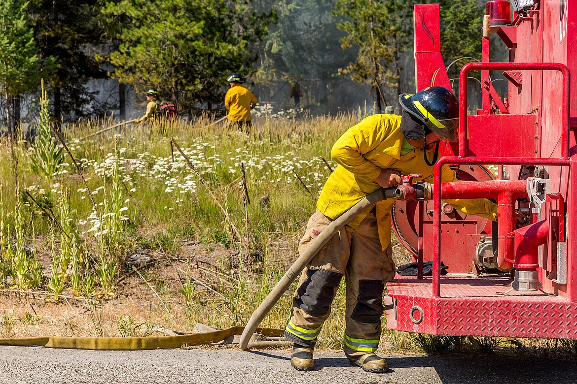 Libby volunteer firefighters Neil Benson mans a water tender while Libby Volunteer Fire Department and U.S. Forest Service firefighters work to extinguish a burning slash pile along Luscher Drive Wednesday. Fire Chief Tom Wood said the fire was a &#147;hold over&#148; from when the pile was burned in May. (John Blodgett/The Western News)