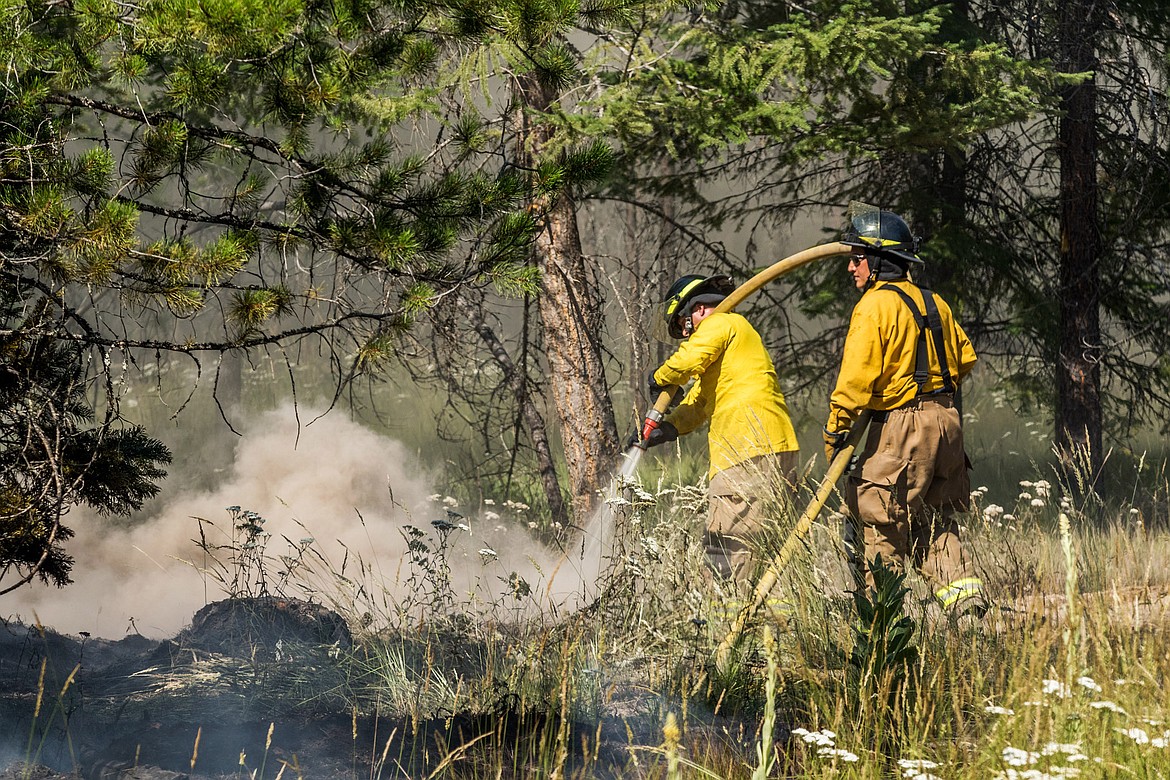 Libby volunteer firefighters Neil Benson and Tom Kim spray water on a burning slash pile along Luscher Drive Wednesday. Fire Chief Tom Wood said the fire was a &#147;hold over&#148; from when the pile was burned in May. (John Blodgett/The Western News)