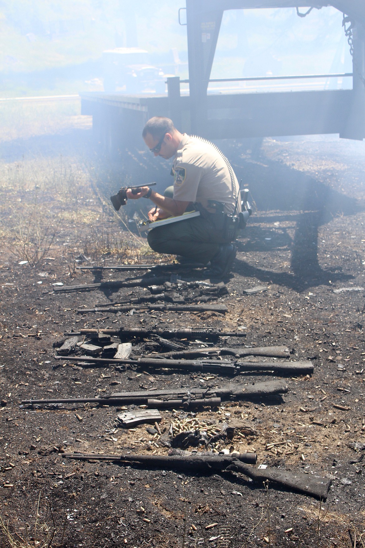 SCSO Captain Jeremy Groves inspects and catalogs several firearms that were burned up in the fire. Ammunition (both whole and exploded) can also be seen scattered about the ground.