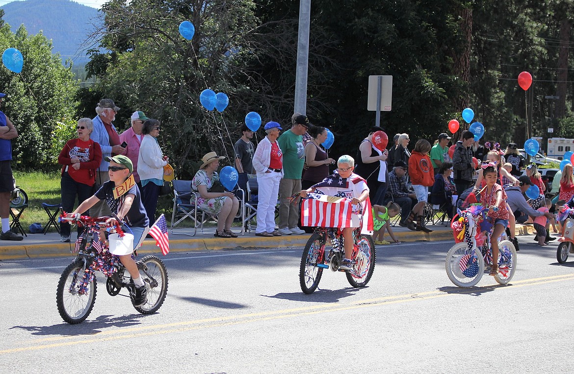 Fourth of July superheroes pedal past the crowd on Old Highway 10 in St. Regis. (Kathleen Woodford/Mineral Independent)