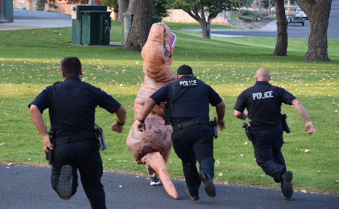 Charles H. Featherstone/Columbia Basin Herald
Police chase 13-year-old Lain Wurl, who wore his dinosaur costume to the lip-sync video shoot in McCosh Park on Thursday, as part of a photo shoot.