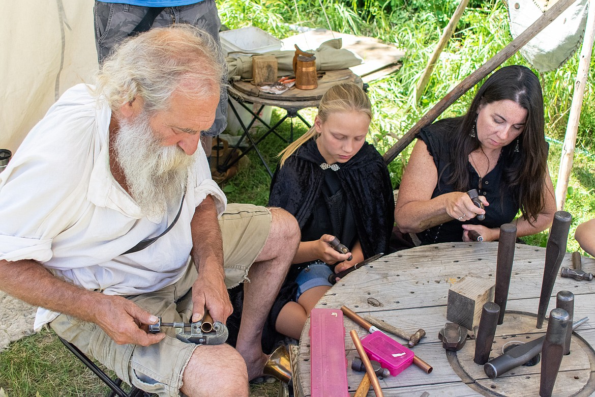 Weezil of Hammered and Twisted by Weezil cuts a piece of copper from a pipe as Ruley Millen and Shelly Haig hammer copper rings to size during the 2018 Kootenai Highlanders Gathering Saturday.