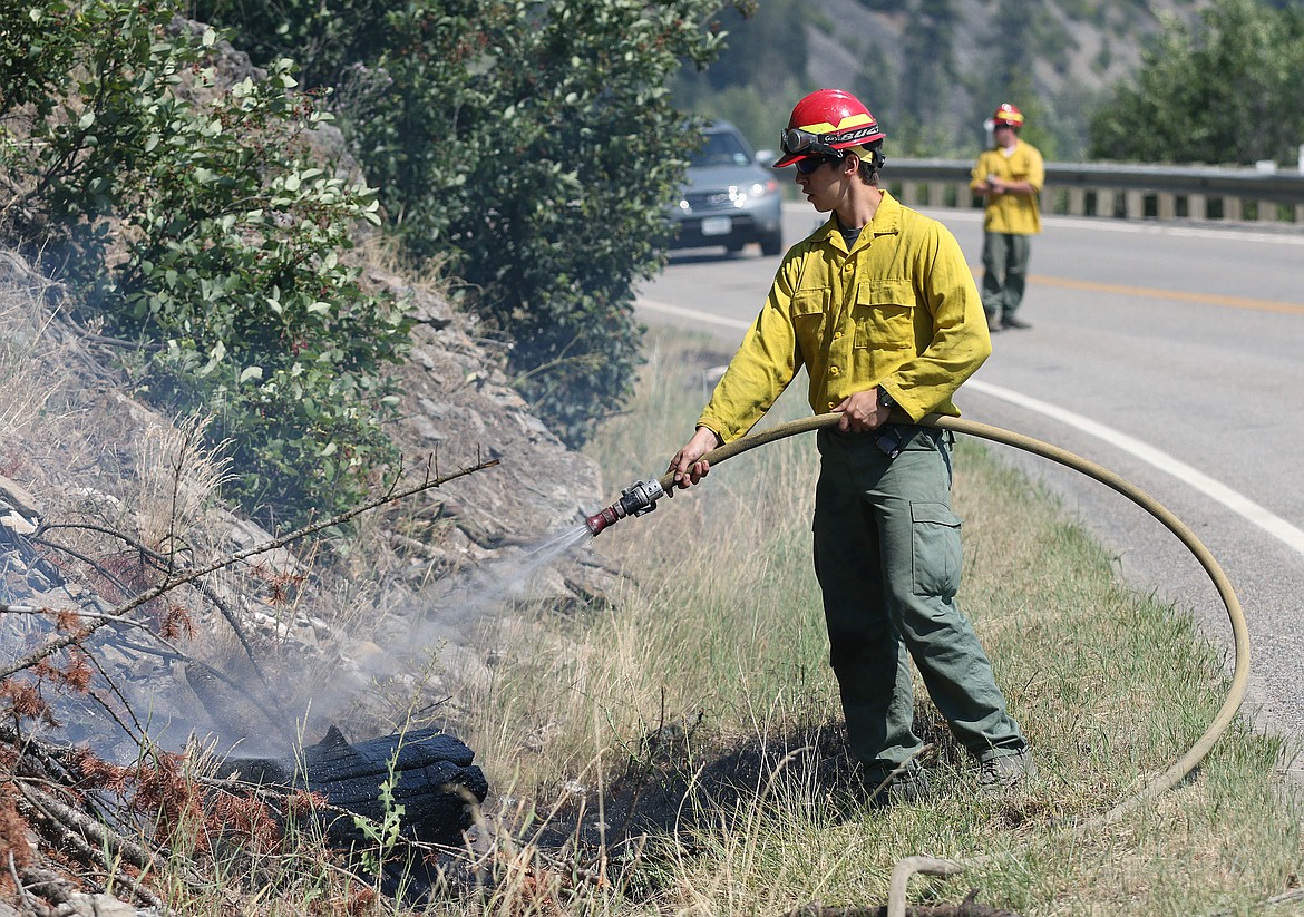 A U.S. Forest Service firefighter douses a burning log that rolled down a slope near milemarker 4 along Highway 37 Friday afternoon. The slope is where the Highway 37 fire began Thursday afternoon. (John Blodgett/The Western News)