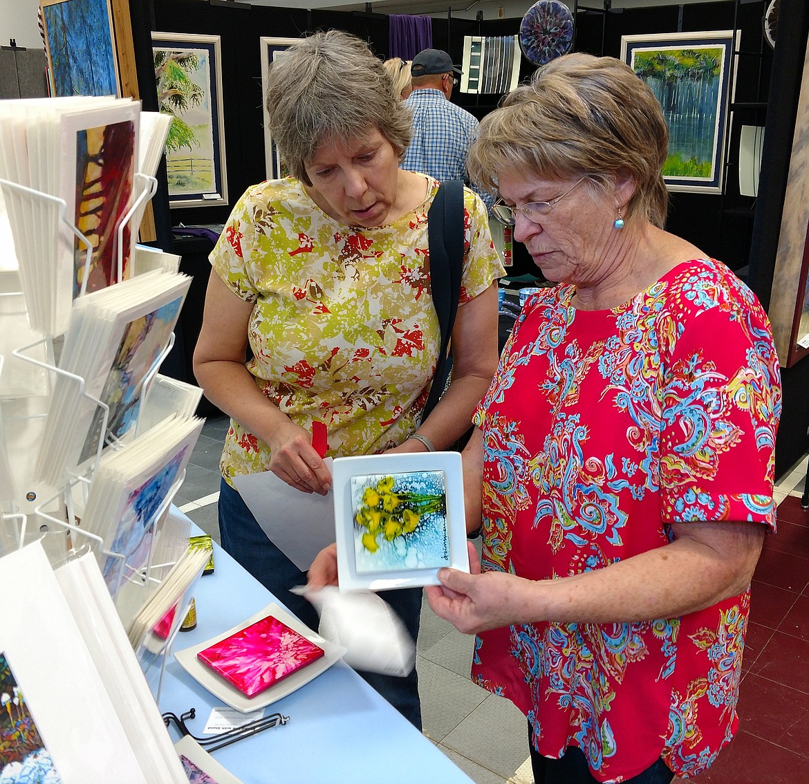 Dianne Zimmerman, right, of Thompson Falls shows her Steamboat Island Art alcohol inks offerings to Karen Olson of Plains during the Artists in Paradise exhibit July 21 during the opening of the Paradise Center. (Joe Sova/Clark Fork Valley Press)