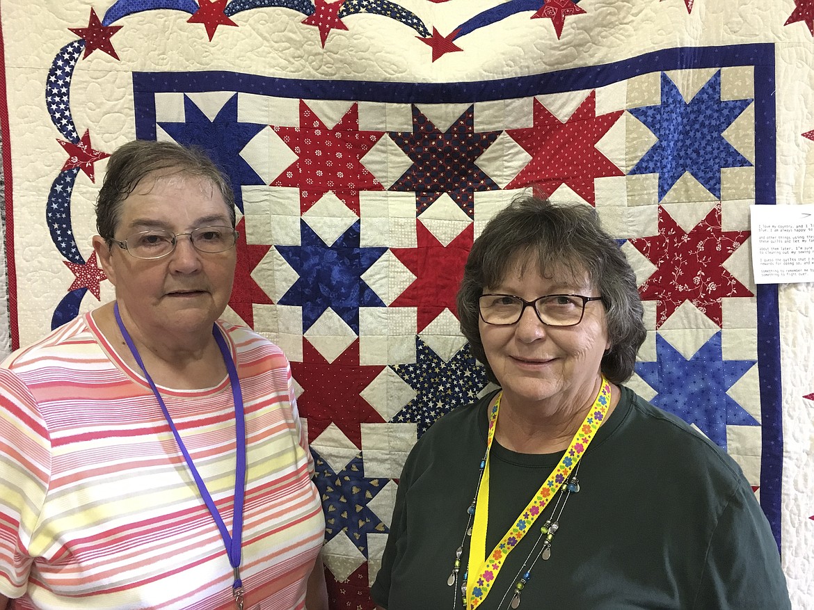 LINDA SCHOON, left, and Rosa Tougas stand in front of a patriotic quilt completed by School at the Mission Mountain Quilt Guild quilt show. The ladies were this year&#146;s featured quilters for the event.