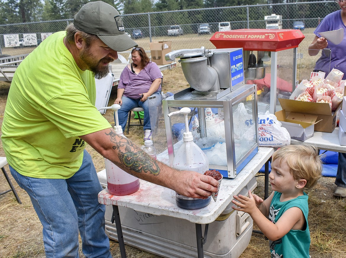 Todd Rebo hands C.J. Gentry a flavored ice during the Three Lakes Roundup outside Troy on Saturday. Though not a member of the Three Lakes Church, Rebo was one of several members of the local Christian community who came out to help with their community outreach. (Ben Kibbey/The Western News)