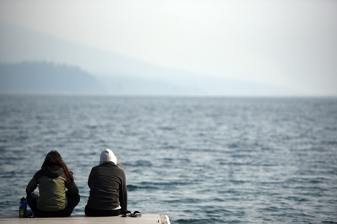 From left, Yaqmur Abay from Turkey and Anne Ruiz from Spain, two summer employees in Glacier National Park sit on the edge of the Apgar dock with the feet in the water of Lake McDonald on Monday morning, August 13. The iconic view into the park has been completely obscured and air quality has been significantly affected by the Howe Ridge, Heaven&#146;s Sake and Numa Ridge fires which are currently burning.
(Brenda Ahearn/Daily Inter Lake)